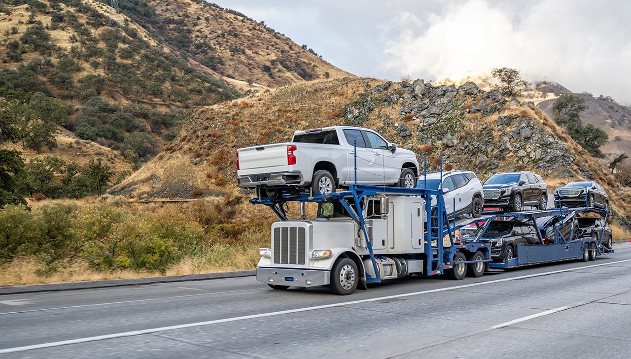 Industrial big rig white car hauler semi truck transporting cars on special two level hydraulic modular semi trailer driving on the highway road with snow mountains hidden in the clouds in California; Shutterstock ID 2237205789; purchase_order: -; job: -; client: -; other: -
